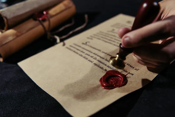 Partial view of ancient chronicler putting wax seal on parchment with manuscript on black table — Stock Photo