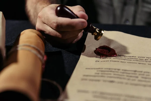 Partial view of medieval monk stamping manuscript with wax seal on blurred foreground and black surface — Stock Photo