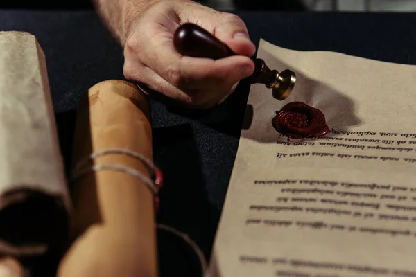 Partial view of monk with wax seal near stamped manuscript and rolled parchments on black surface — Stock Photo