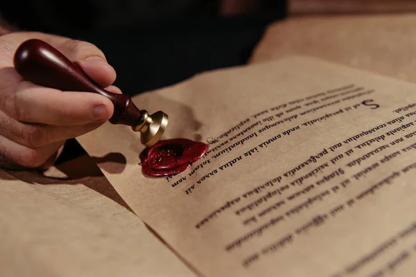 Cropped view of monk with wax seal near ancient manuscript isolated on black — Stock Photo