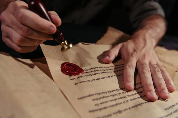 Partial view of abbot approving ancient manuscript with wax seal on black background — Stock Photo