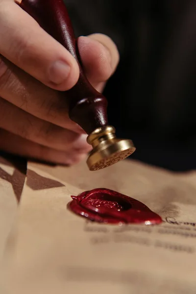 Nahaufnahme von Wachssiegel in der Hand eines abgeschnittenen Priesters in der Nähe von Pergament isoliert auf schwarz — Stockfoto