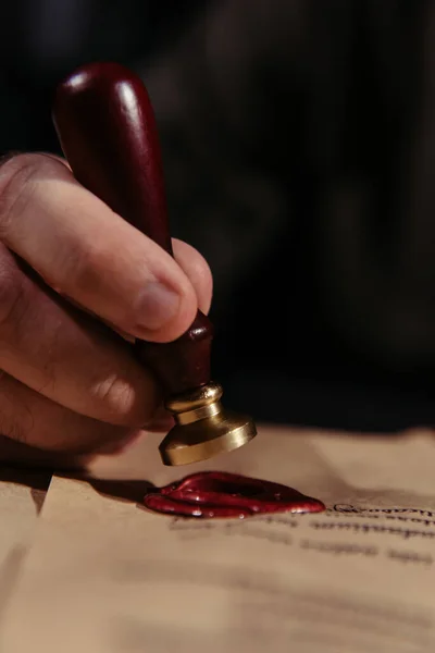 Partial view of priest with wax seal near medieval chronicle on parchment isolated on black — Stock Photo