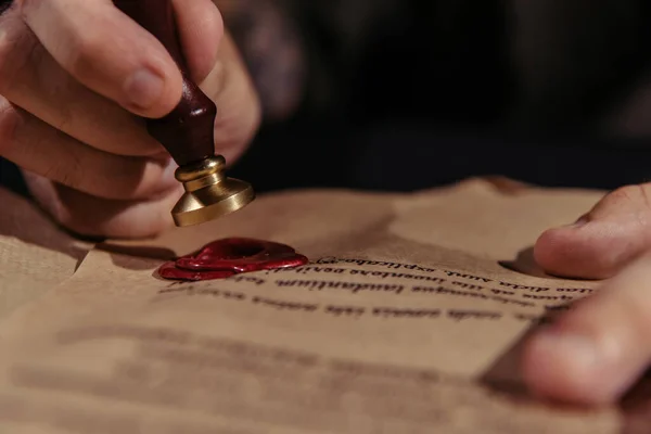 Close up view of wax seal in hand of cropped monk near manuscript on black background — Stock Photo