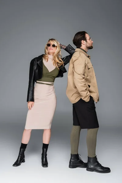 Full length of stylish couple in autumnal outfits and posing together on grey — Photo de stock