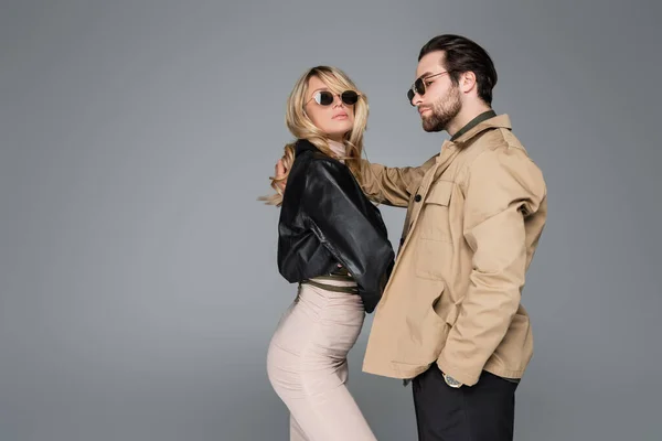 Blonde woman in leather jacket and bearded man in sunglasses posing together isolated on grey — Fotografia de Stock