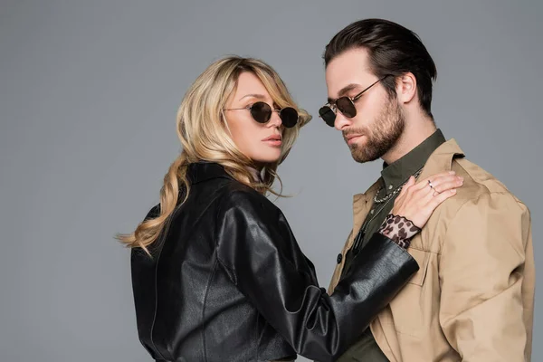 Blonde in stylish black jacket woman hugging bearded man in sunglasses isolated on grey — Foto stock