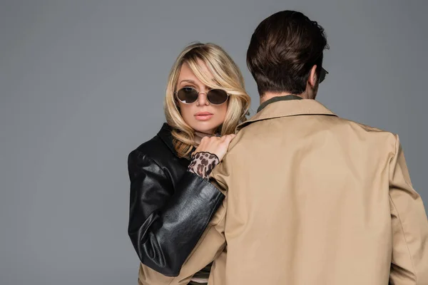 Blonde in stylish leather jacket woman and sunglasses hugging man isolated on grey — Photo de stock
