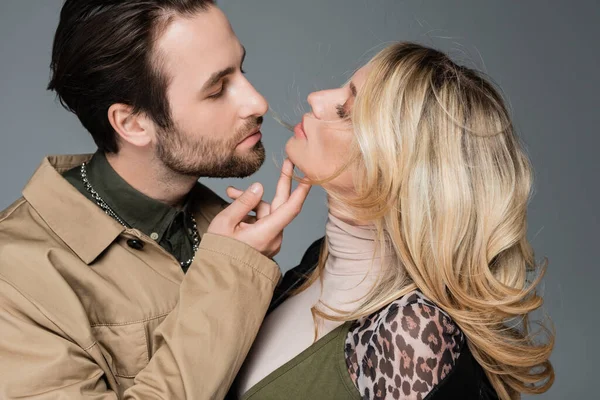 Stylish bearded man touching chin of blonde woman while flirting isolated on grey — Foto stock