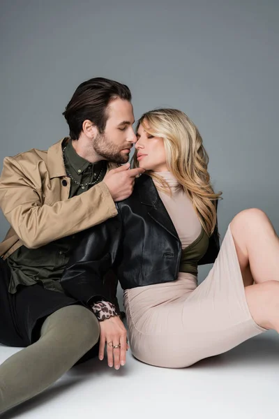 Stylish bearded man touching chin of blonde woman while sitting on grey — Photo de stock