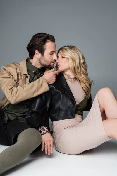 Stylish bearded man touching chin of blonde woman while sitting on grey — Fotografia de Stock