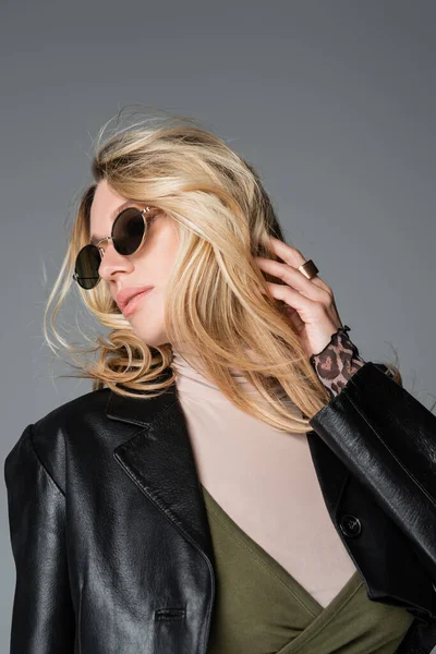 Blonde woman in black leather jacket and stylish sunglasses posing isolated on grey — Fotografia de Stock