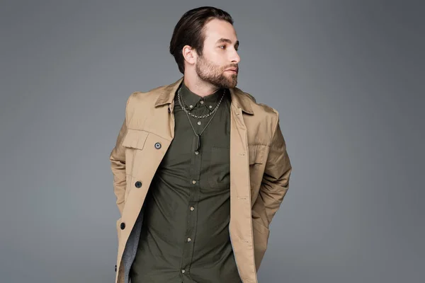 Bearded man in beige jacket and green shirt looking at camera isolated on grey — Stockfoto