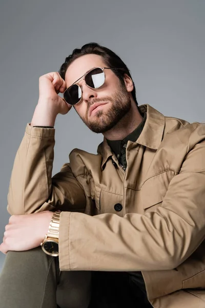 Bearded man in stylish jacket and sunglasses looking at camera isolated on grey — Stockfoto