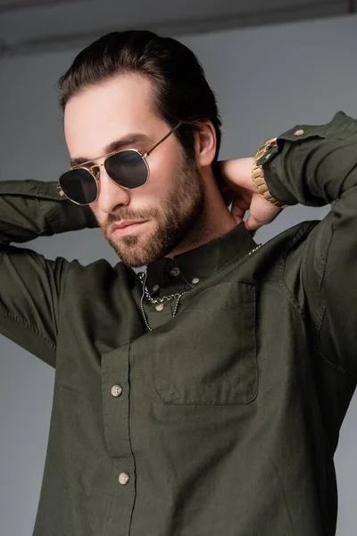 Bearded man in stylish green shirt and sunglasses posing on grey — Stockfoto