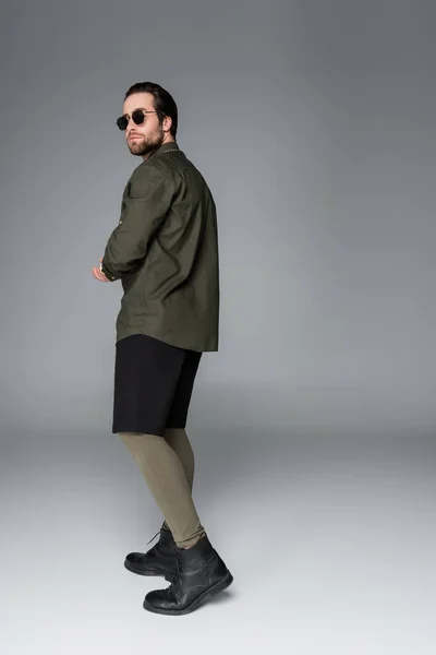 Full length of bearded man in sunglasses and stylish outfit posing on grey — Stockfoto