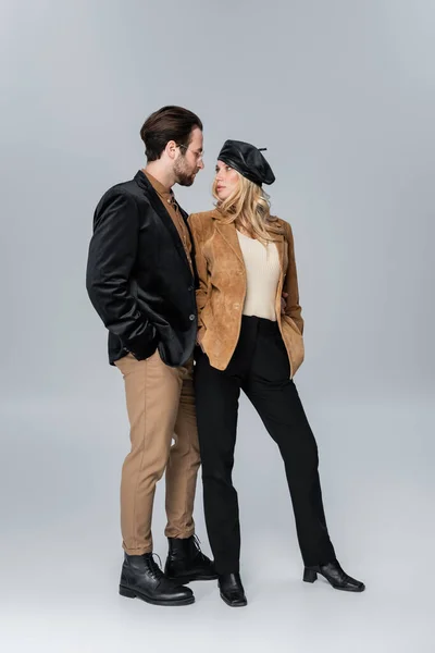 Full length of stylish woman in black beret near bearded man in sunglasses posing on grey — Stockfoto