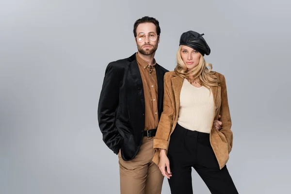 Blonde woman in stylish beret posing with bearded man in sunglasses isolated on grey — Foto stock