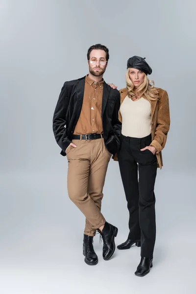 Full length of blonde woman in stylish beret near bearded man in sunglasses posing on grey — Stockfoto