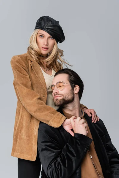 Blonde woman in stylish beret hugging bearded man in sunglasses isolated on grey — Photo de stock