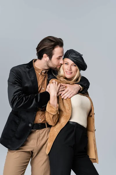 Cheerful man hugging happy woman in stylish beret isolated on grey — Foto stock