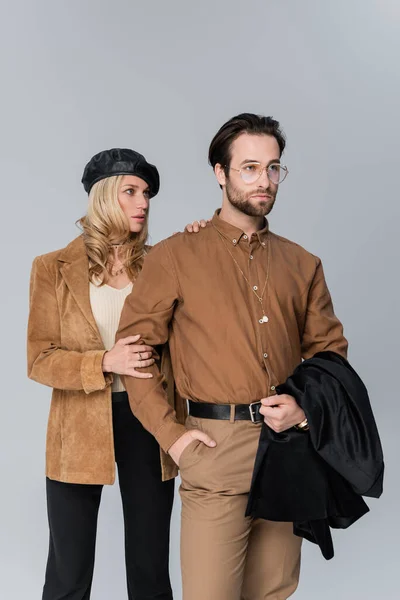 Blonde woman in stylish beret hugging bearded man in sunglasses and posing on grey — Photo de stock