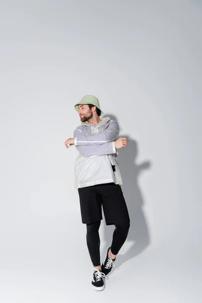 Повна довжина бородатого чоловіка в модному спортивному вбранні і панамському капелюсі позує на сірий — стокове фото