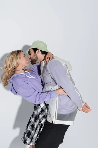 Bearded man in panama hat kissing happy blonde girlfriend in tartan skirt on grey — Photo de stock