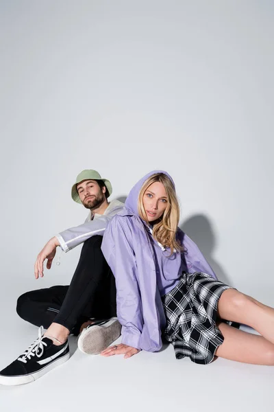 Full length of woman in tartan skirt sitting with man in panama hat on grey — Stockfoto