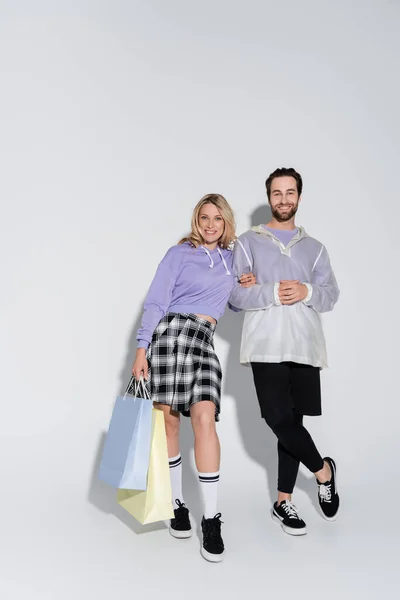 Full length of happy and stylish couple holding shopping bags on grey — Stockfoto