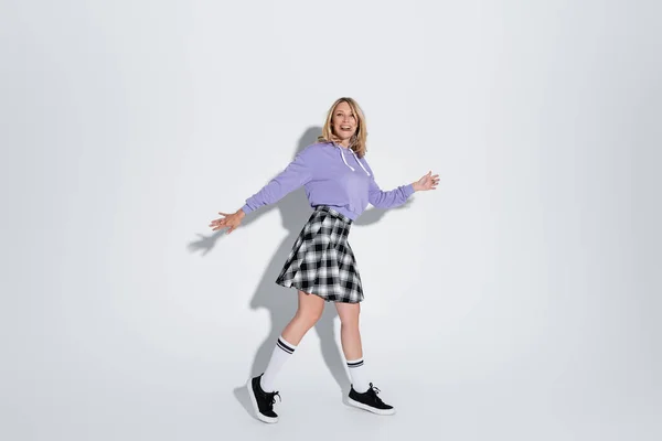 Full length of excited blonde woman in trendy outfit posing with outstretched hands on grey — Stock Photo