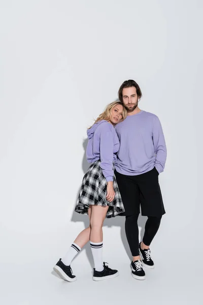 Full length of bearded man posing with blonde woman in tartan skirt on grey — Stockfoto