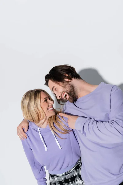 Happy bearded man in purple sweatshirts pointing at blonde woman on grey — Fotografia de Stock