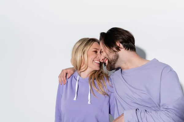 Happy bearded man in purple sweatshirts smiling with blonde woman on grey — Stockfoto