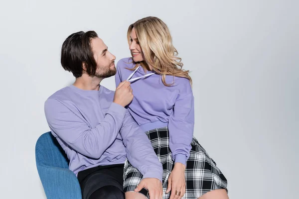 Cheerful man and blonde woman in tartan skirt sitting on blue armchair isolated on grey — Foto stock