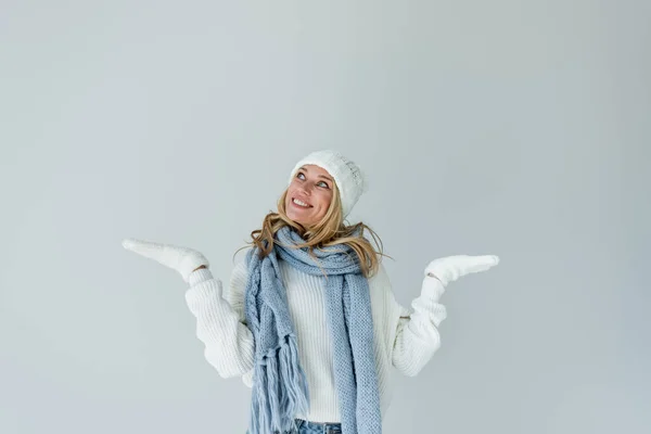 Happy blonde woman in winter hat and knitted scarf gesturing isolated on grey — Foto stock