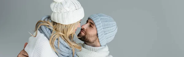 Блондинка в вязаной шляпе смотрит на бородатого бойфренда в зимнем наряде, изолированном на сером, баннер — стоковое фото