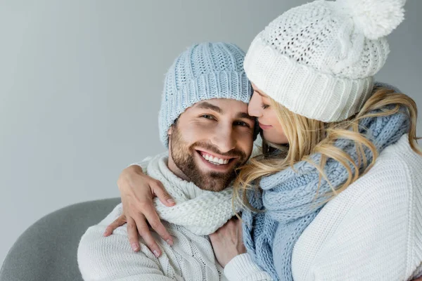 Blonde woman in knitted hat hugging with smiling boyfriend in winter outfit isolated on grey — Fotografia de Stock