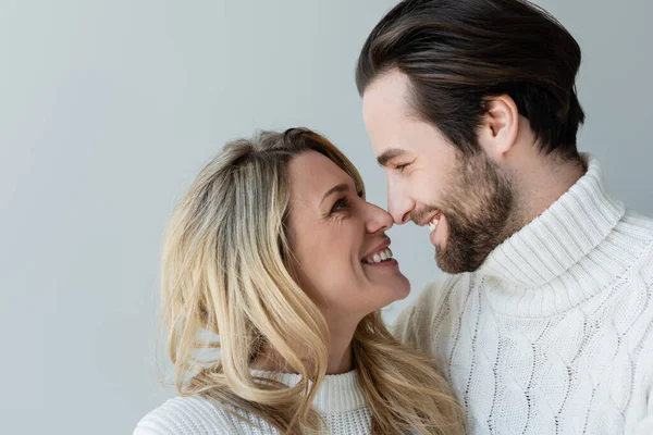 Портрет веселой пары в вязаных белых свитерах, улыбающихся, глядя друг на друга, изолированных на сером — стоковое фото