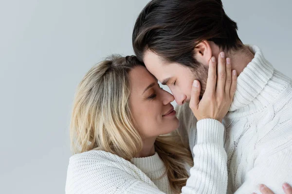 Portrait of cheerful couple in knitted white sweaters smiling while hugging isolated on grey — Fotografia de Stock