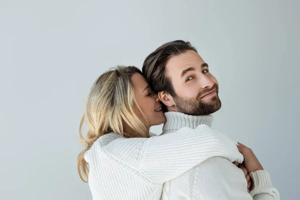 Cheerful blonde woman in white knitted sweater hugging bearded man isolated on grey — Stock Photo