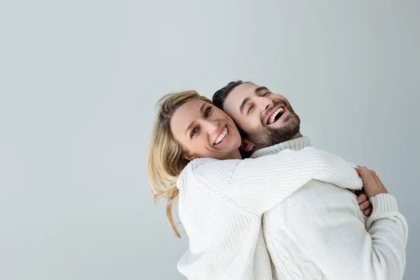 Positive blonde woman in white knitted sweater hugging bearded man isolated on grey — Stock Photo