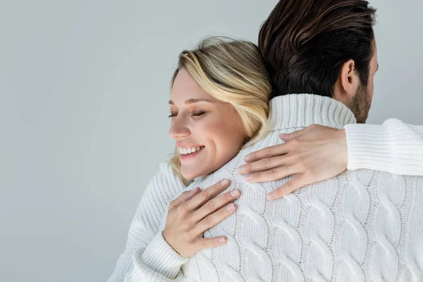 Cheerful blonde woman in white sweater hugging back of boyfriend isolated on grey — Fotografia de Stock