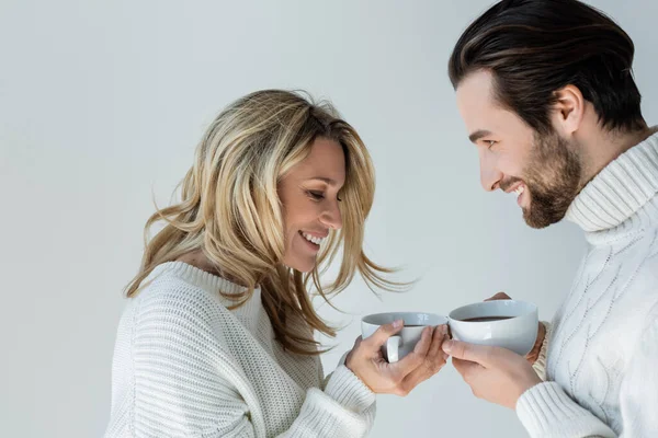 Happy man and woman in white knitted sweaters holding cups of coffee isolated on grey — Stock Photo