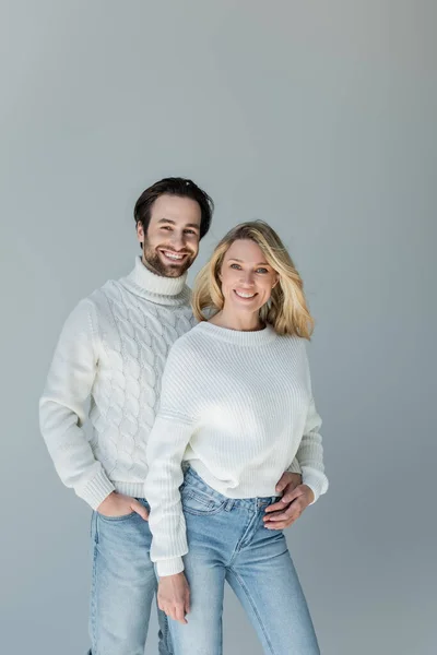 Cheerful man standing with hand in pocket and hugging blonde girlfriend in sweater isolated on grey — Stockfoto