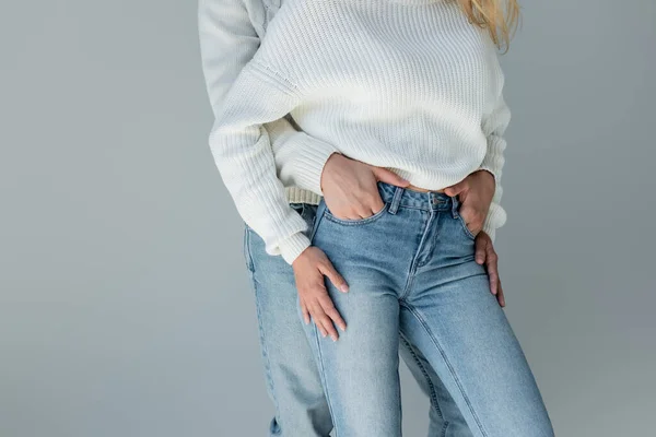 Cropped view of couple in white sweaters and jeans posing isolated on grey — Stock Photo