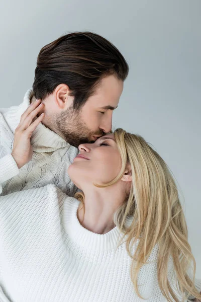 Bearded man kissing forehead of blonde girlfriend in sweater isolated on grey — Stockfoto