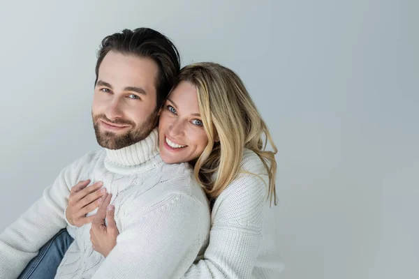 Cheerful woman hugging bearded man in white sweater and looking at camera isolated on grey — Stock Photo