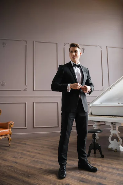 Man in suit adjusting jacket near piano at home — Stock Photo