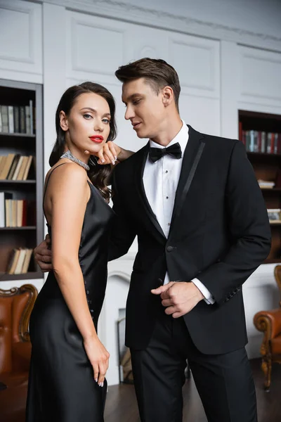 Elegant man in suit looking at girlfriend in silk dress at home — Photo de stock